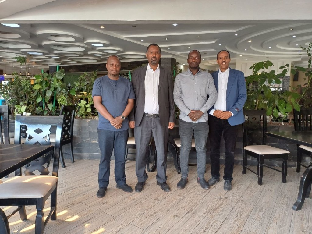 Four men in business attire posing in a bright modern indoor space.