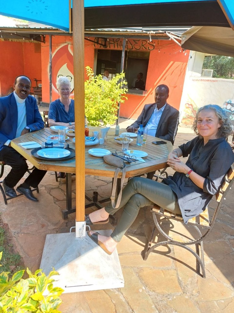 Four colleagues seated around an outdoor table under a blue umbrella.